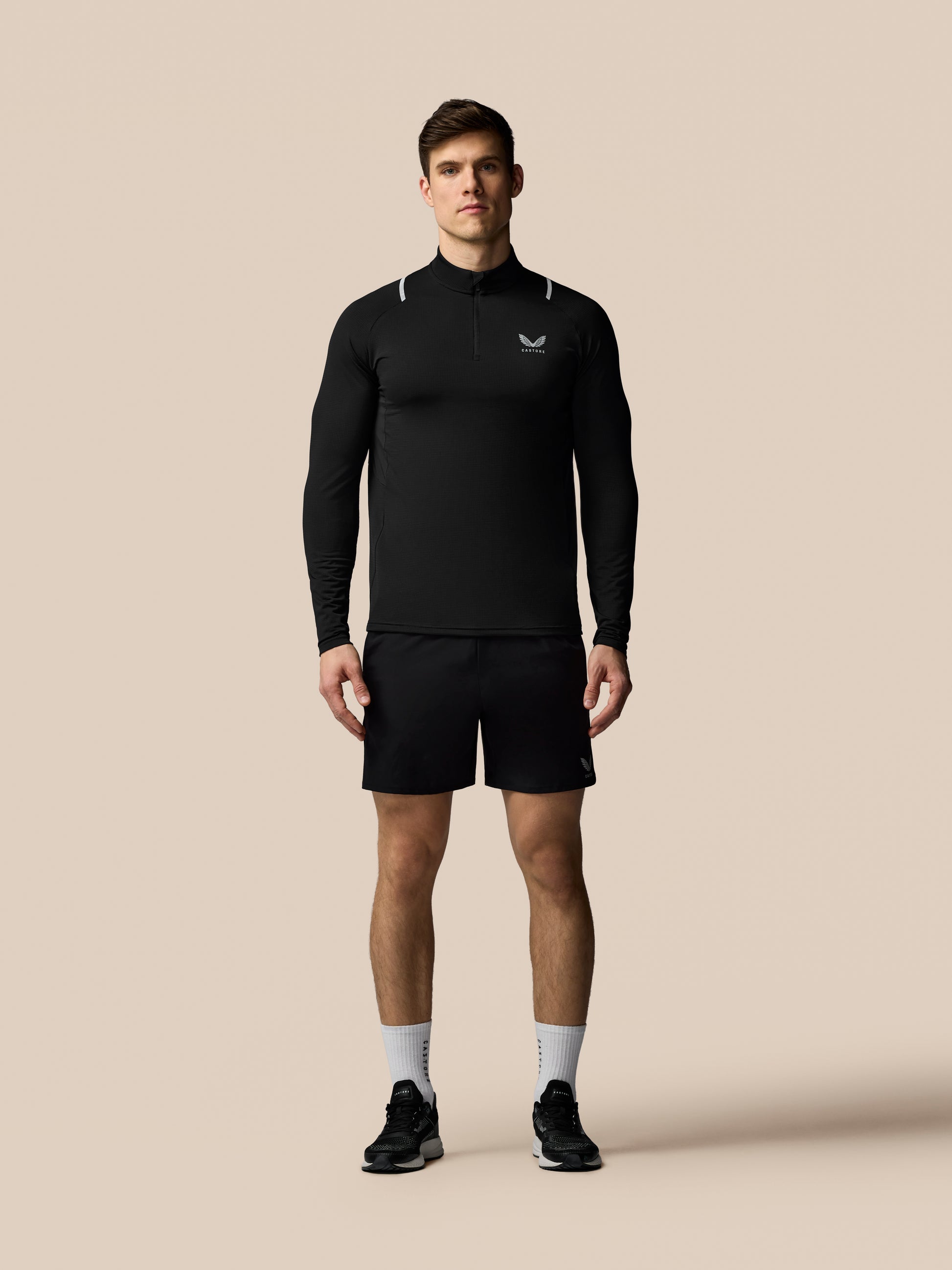 Male model in black Apex Training 1/4 zip top with long sleeves, high collar, reflective shoulder accents and Castore logo on chest