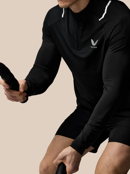 Close up of a man wearing a black Castore Apex Training 1/4 Zip top with reflective white shoulder stripes and chest logo.