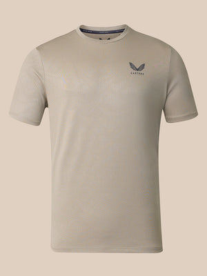 A light beige short-sleeve athletic t-shirt with a subtle ribbed texture, featuring a dark gray wing logo and the brand name 'CASTORE' On the left chest, displayed against a solid beige background.