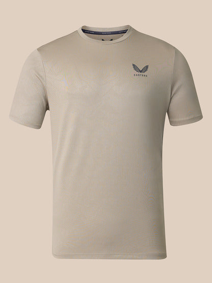 A light beige short-sleeve athletic t-shirt with a subtle ribbed texture, featuring a dark gray wing logo and the brand name 'CASTORE' On the left chest, displayed against a solid beige background.
