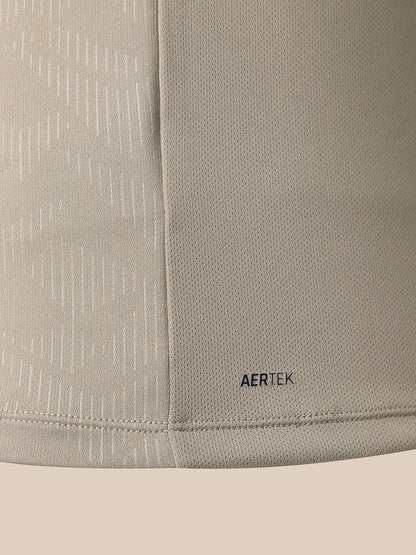 Close-up of a light beige athletic fabric with a subtle vertical textured pattern and a small black AERTEK logo near the bottom hem.