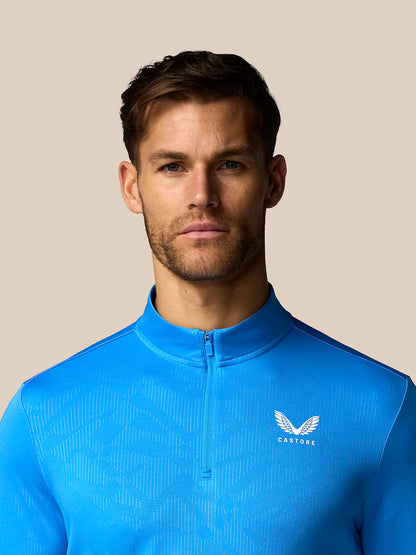 Man wearing a blue athletic jacket with a logo on a beige background