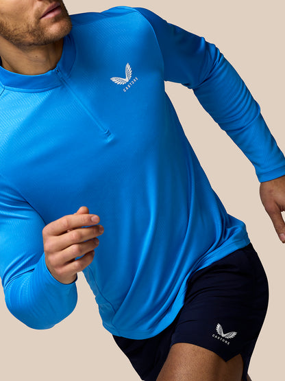 Male model wearing blue Castore Adapt All-Over Print Quarter Zip Long Sleeve Top in action with chest logo