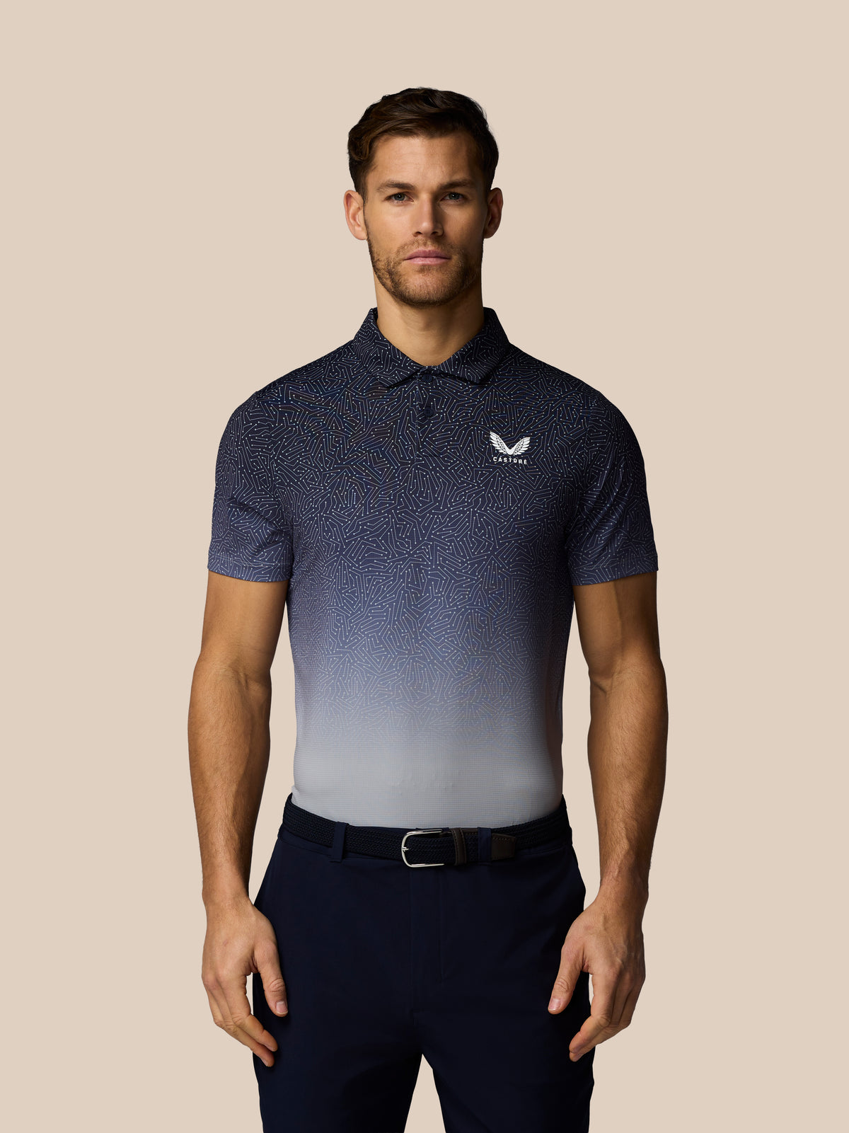Man wearing a navy blue patterned polo shirt with a logo on a beige background