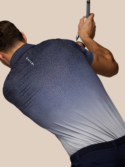 Back view of a golfer wearing a navy map-printed Castore polo during a swing.