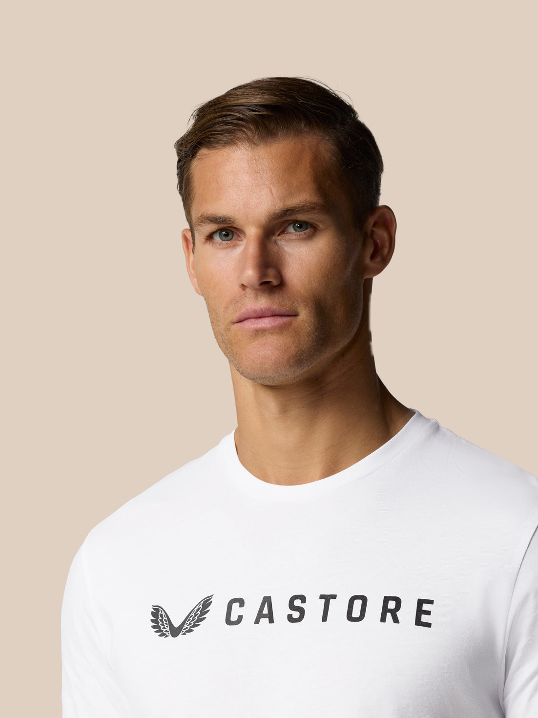 Head and shoulders shot of a male model wearing a white Castore Graphic Lifestyle T-Shirt with the Castore wordmark across the chest