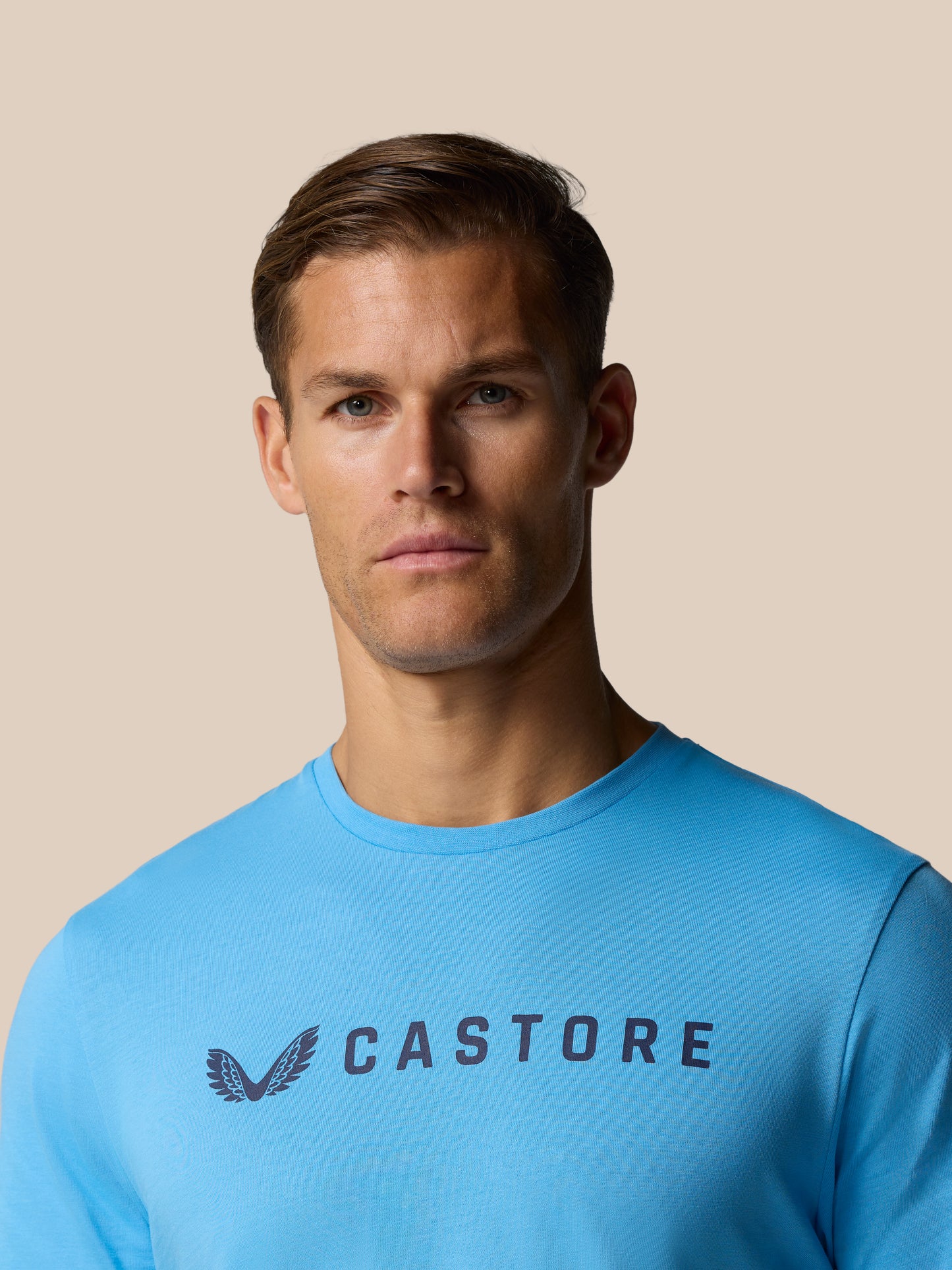 Close up of a man wearing a blue Castore graphic T shirt with the logo and wing emblem on the chest