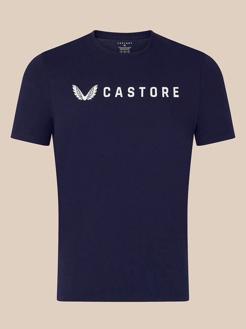 A navy blue short-sleeve crewneck t-shirt with a white Castore wing logo and brand name printed across the chest, displayed against a solid beige background.
