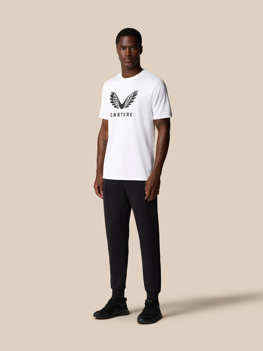 Front three quarter view of a male model wearing a white Castore graphic training T shirt with wing logo