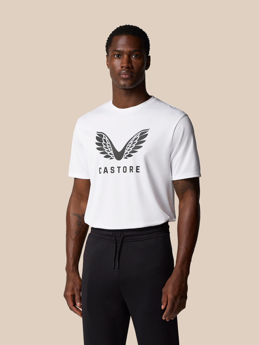 Front view of a male model wearing a white Castore graphic training T shirt with a large wing logo across the chest