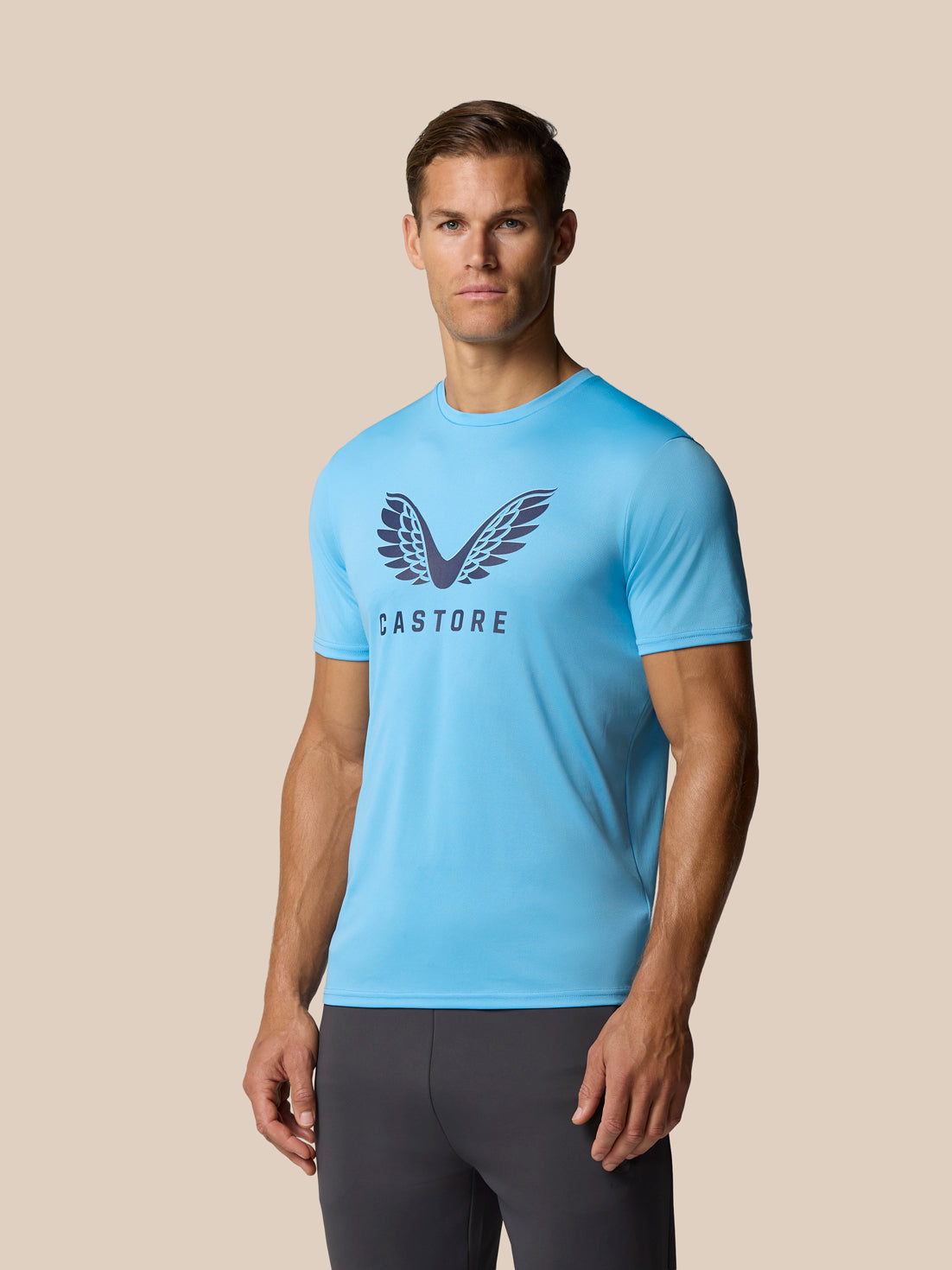 Model wearing blue Castore graphic T shirt with wings logo on the chest