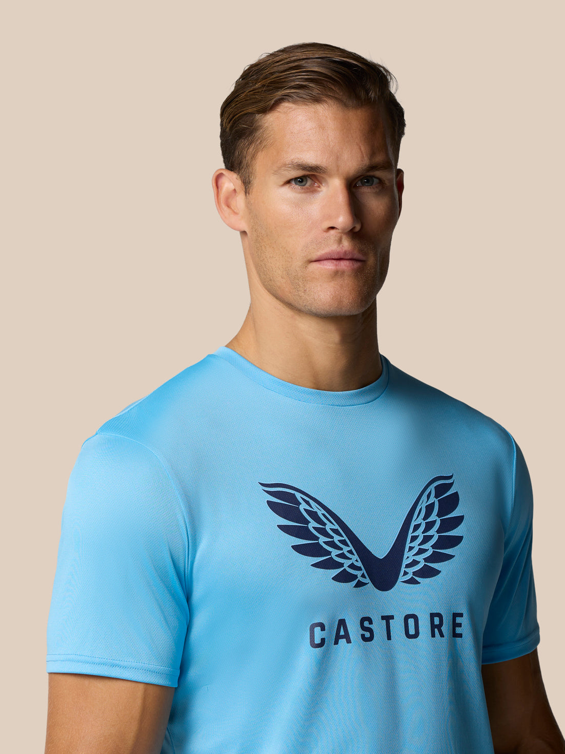 Front view of a man in a light blue graphic training T shirt with Castore wings logo on chest