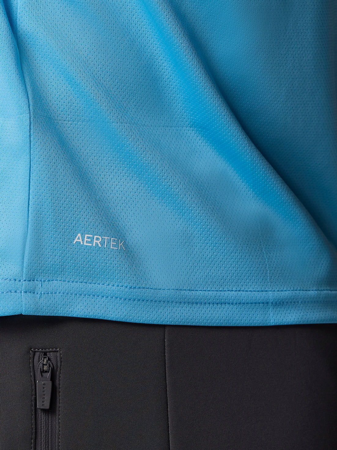 Close up of blue AerTek knit fabric with seam detail and a black zip pocket visible below