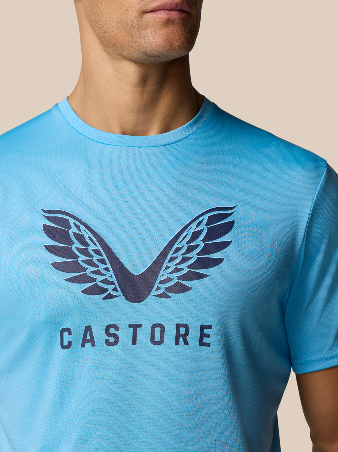 Close-up of a man wearing a light blue Castore Graphic Training T-Shirt with the wing logo and CASTORE lettering on the chest.