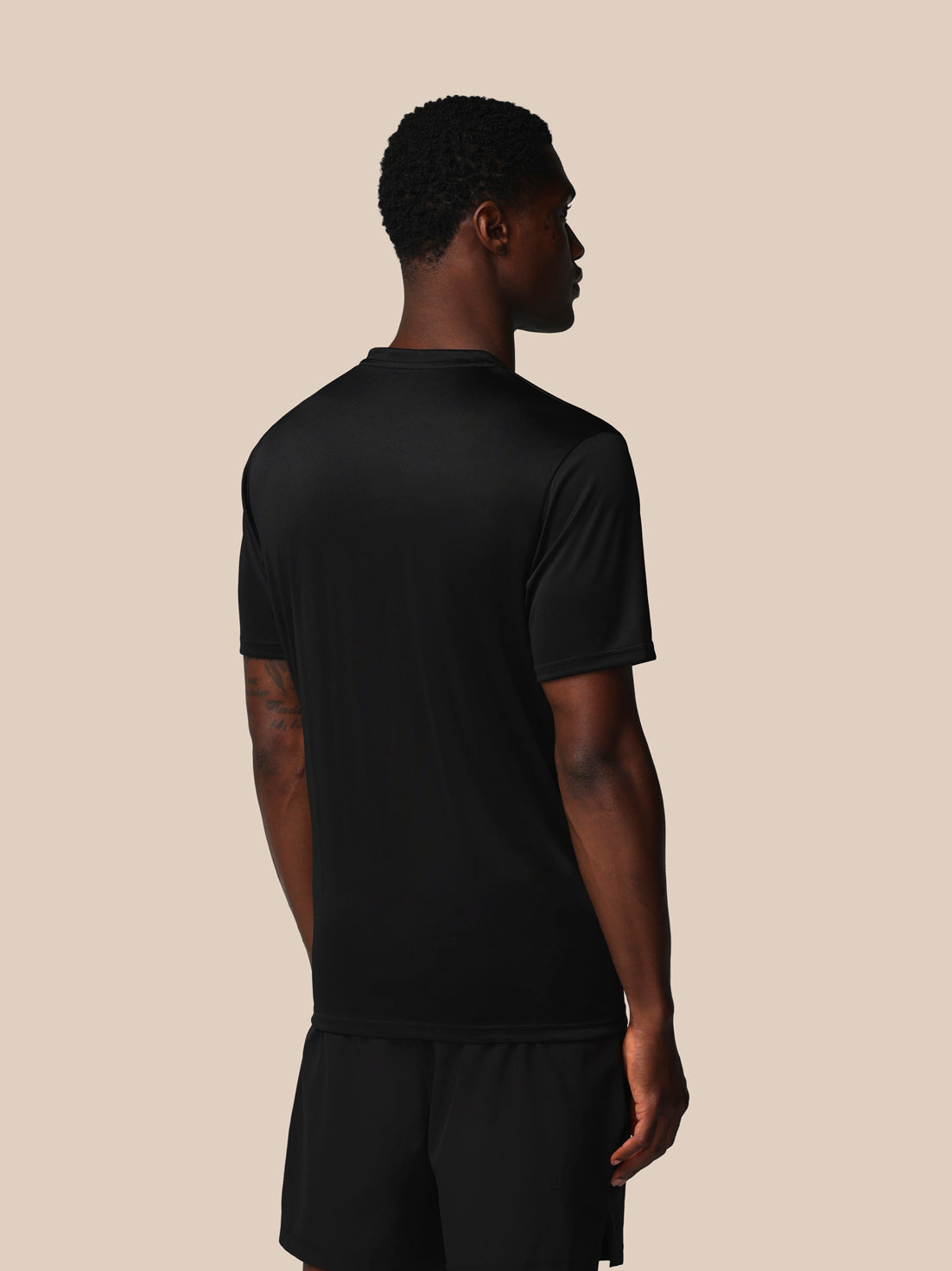 Person wearing a black t-shirt and shorts on a beige background
