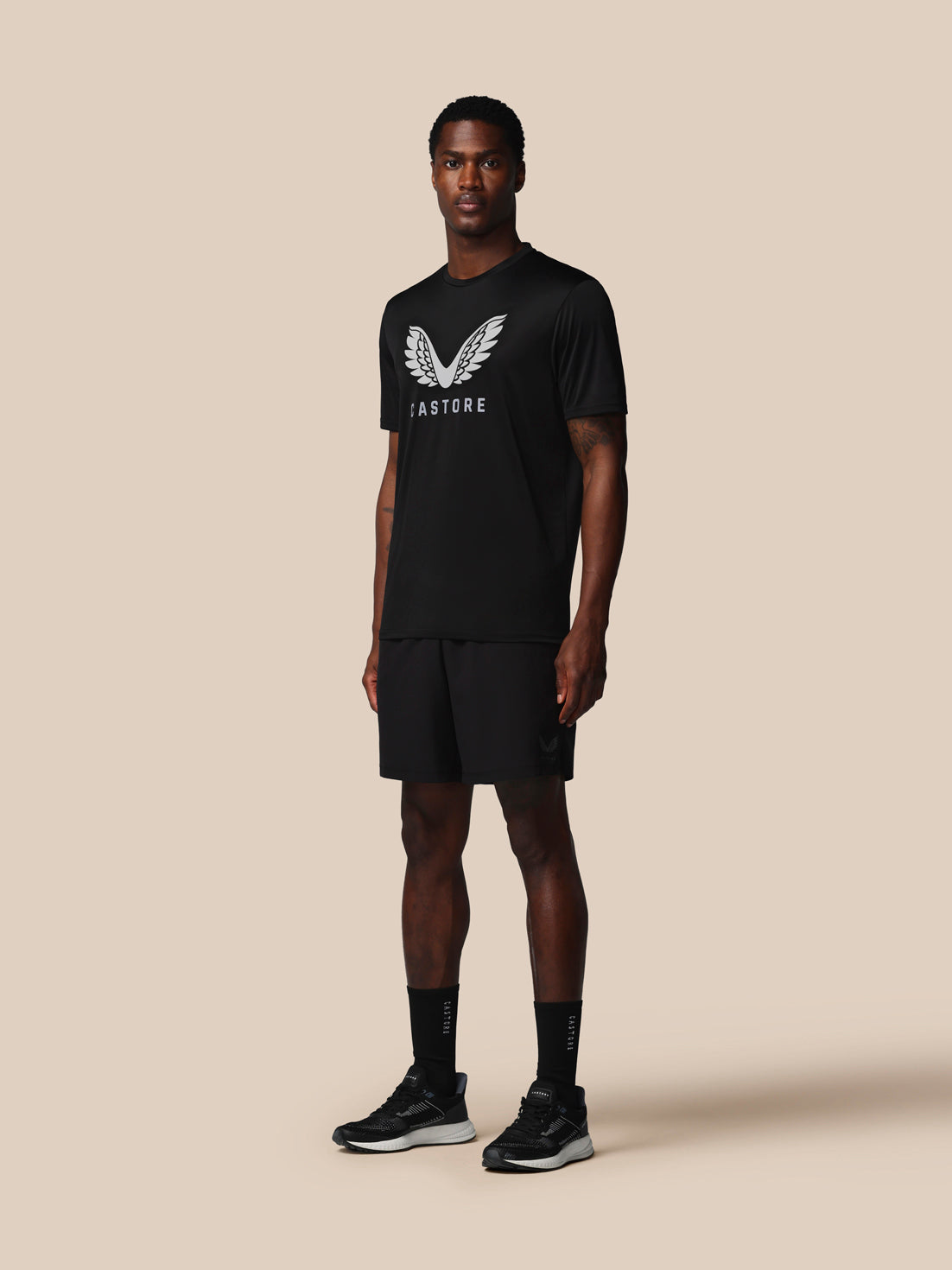 Person wearing a black t-shirt and shorts with a logo on a beige background