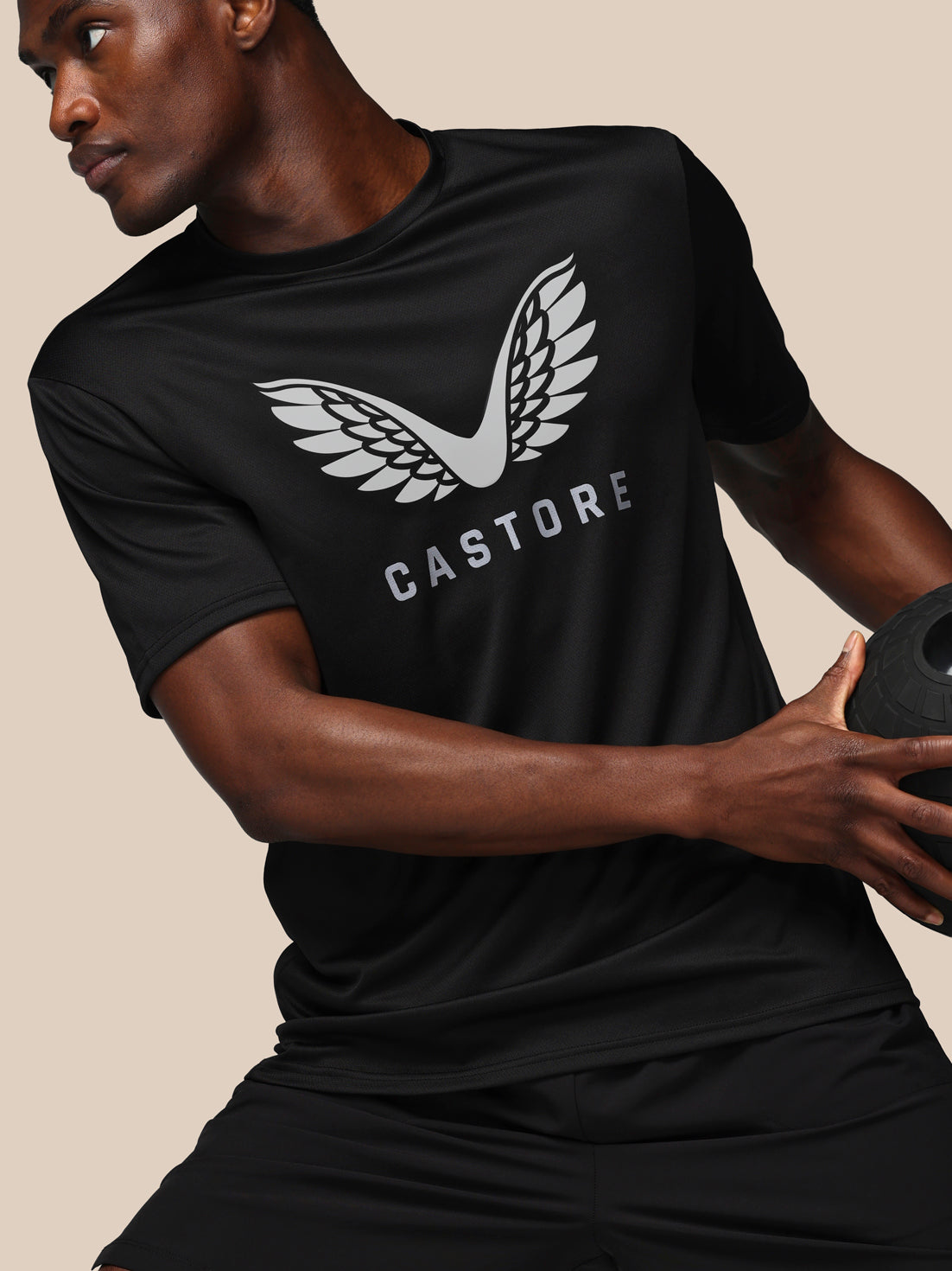 Person wearing a black t-shirt with 'Castore' logo holding a medicine ball.