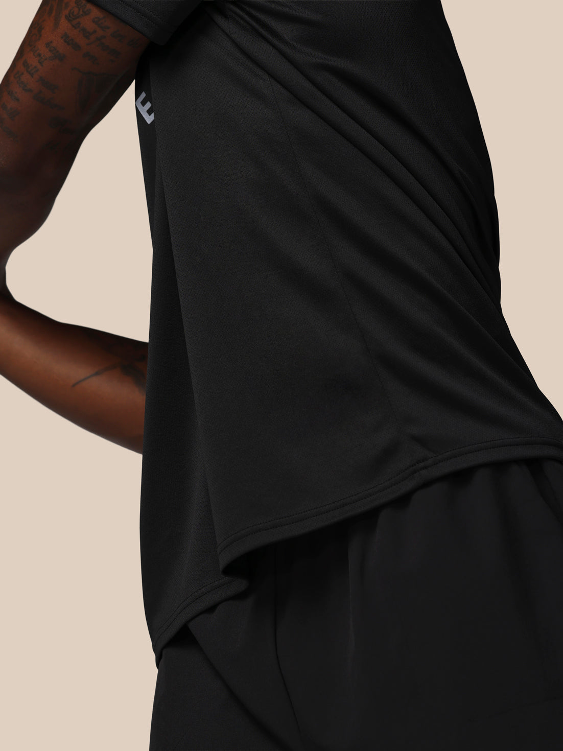 Person wearing a black outfit with a visible brand logo on a beige background
