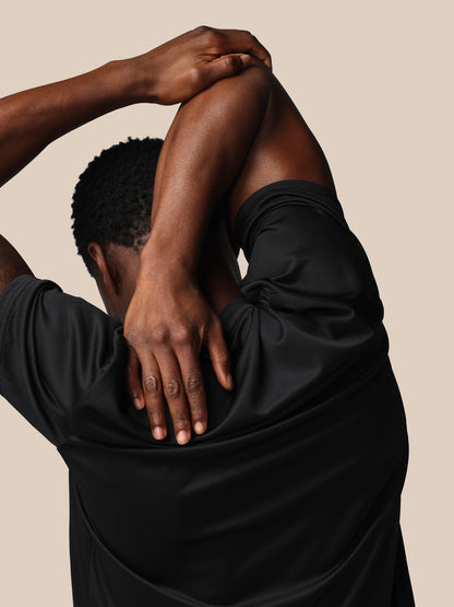 Person wearing a black shirt with hands on the back against a beige background