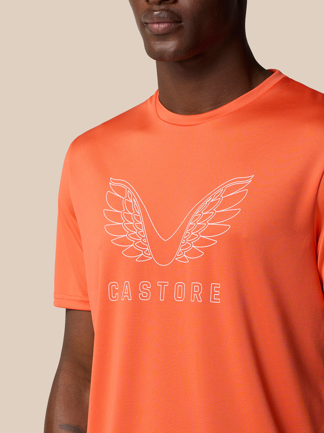 Close-up of bright orange Castore graphic training T shirt showing large white wing logo and CASTORE text across the chest.