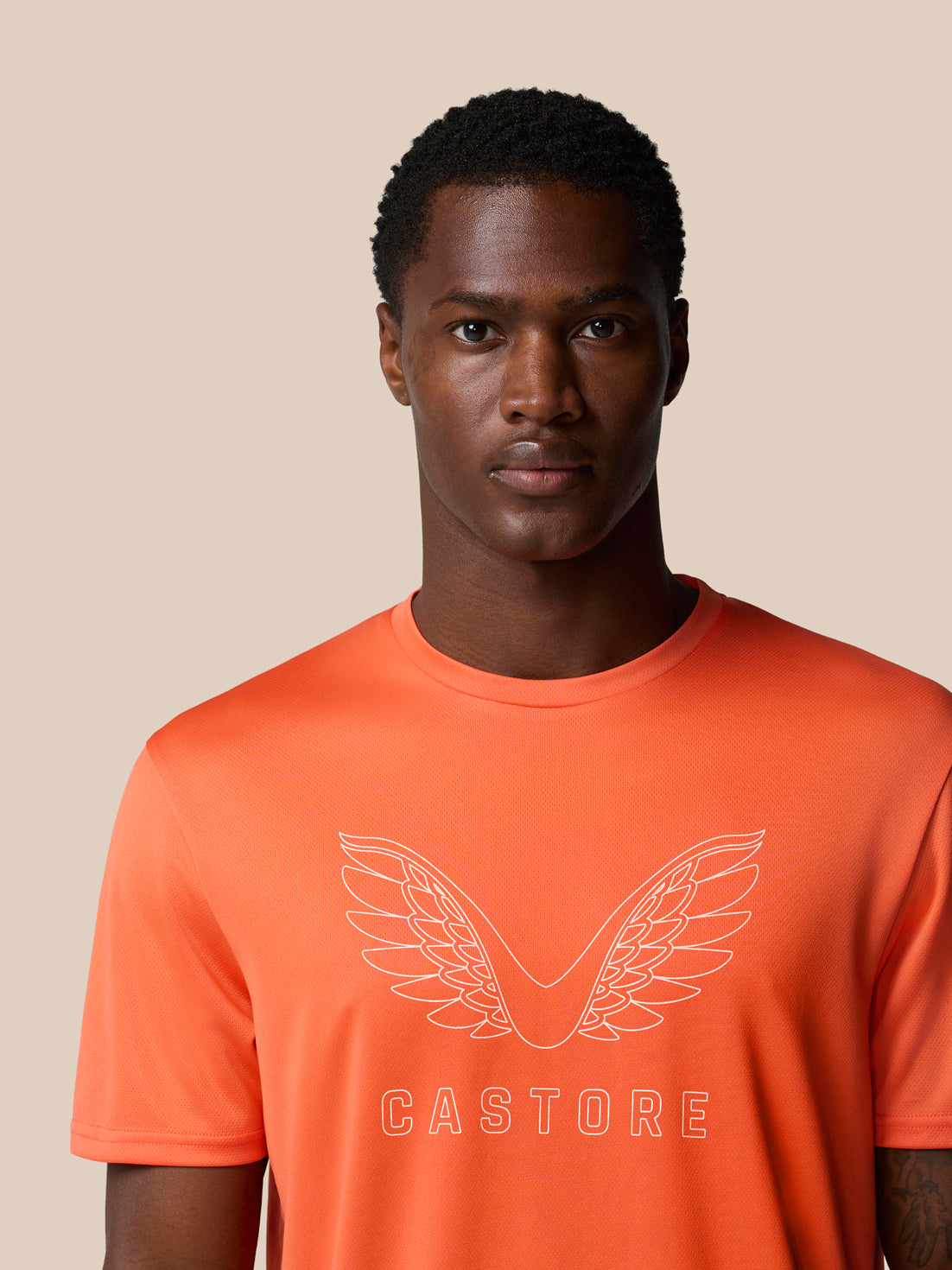Shoulder and chest view of bright orange Castore graphic training T shirt with white wing logo and CASTORE branding.
