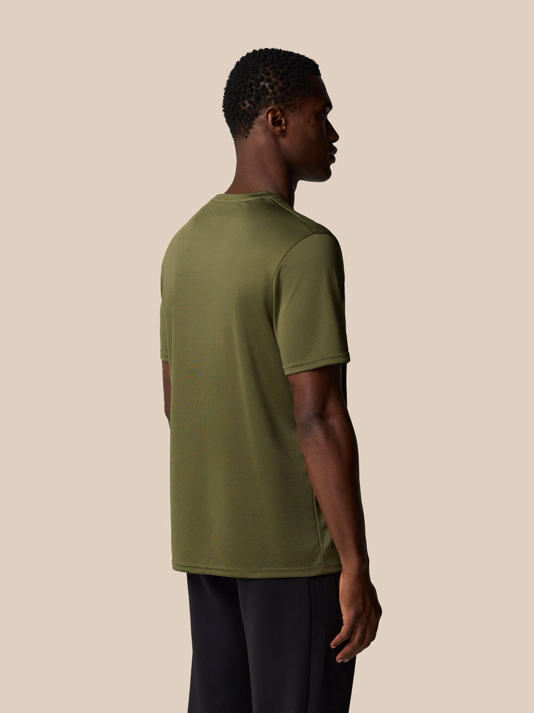 Back view of a male model wearing ivy green short sleeve training t shirt against a beige backdrop