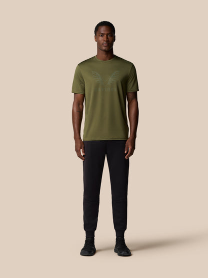 Male model wearing ivy green graphic training T-shirt with wing emblem and Castore logo, paired with black joggers.