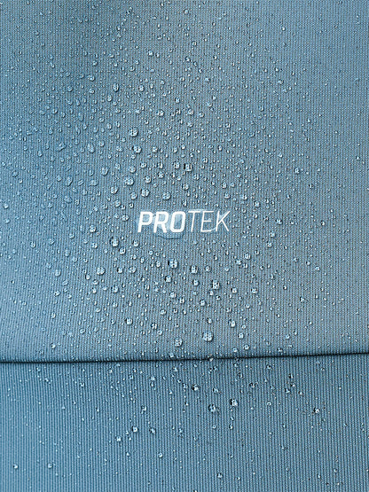 Close-up of a blue-gray textured fabric covered in water droplets, with the word PROTEK printed in white at center. The image demonstrates a water-resistant or protective finish.