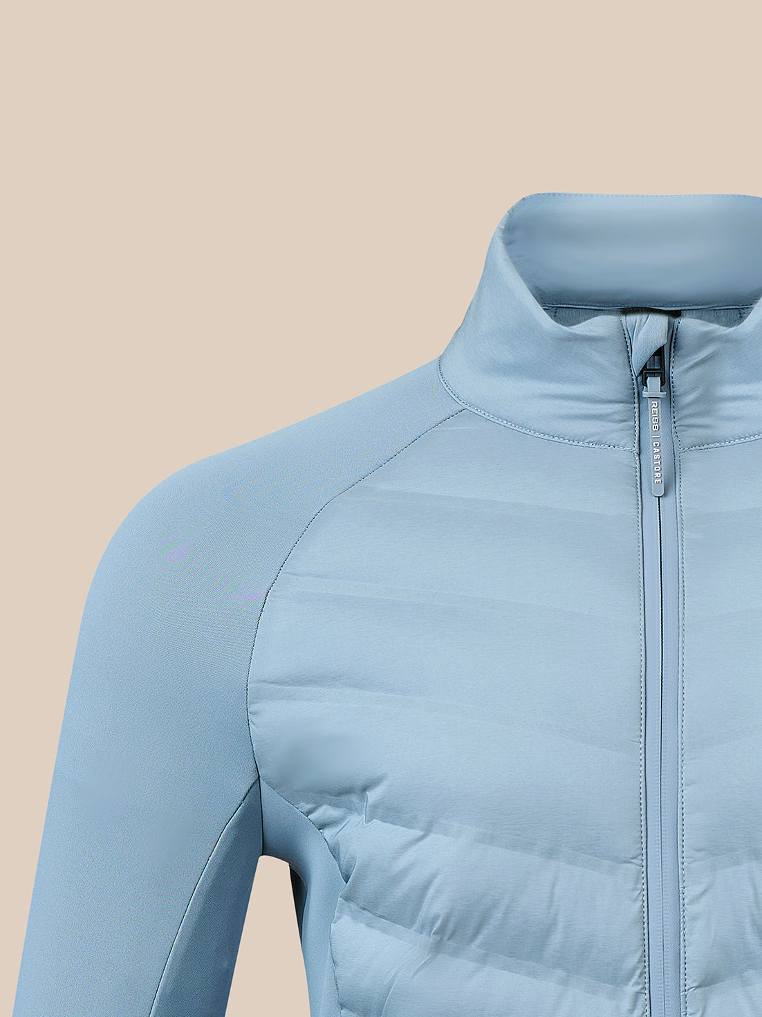 A close-up of a light blue puffer jacket with a high collar and front zipper, shown against a solid beige background.