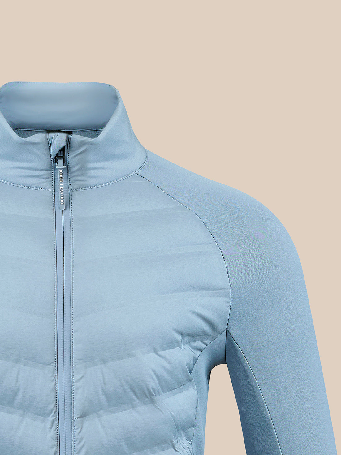 A close-up of a light blue puffer jacket with a high collar and front zipper, shown against a solid beige background.