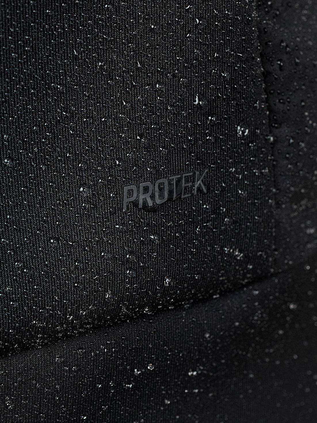 Close up of water droplets beading on black Protek fabric of the gilet.