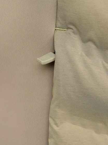 Close-up detail of a garment showing a ribbed fabric panel in a muted dusty pink next to a smooth quilted panel in a light beige/taupe color, joined by a small gold stitch and featuring a small white plastic tab.