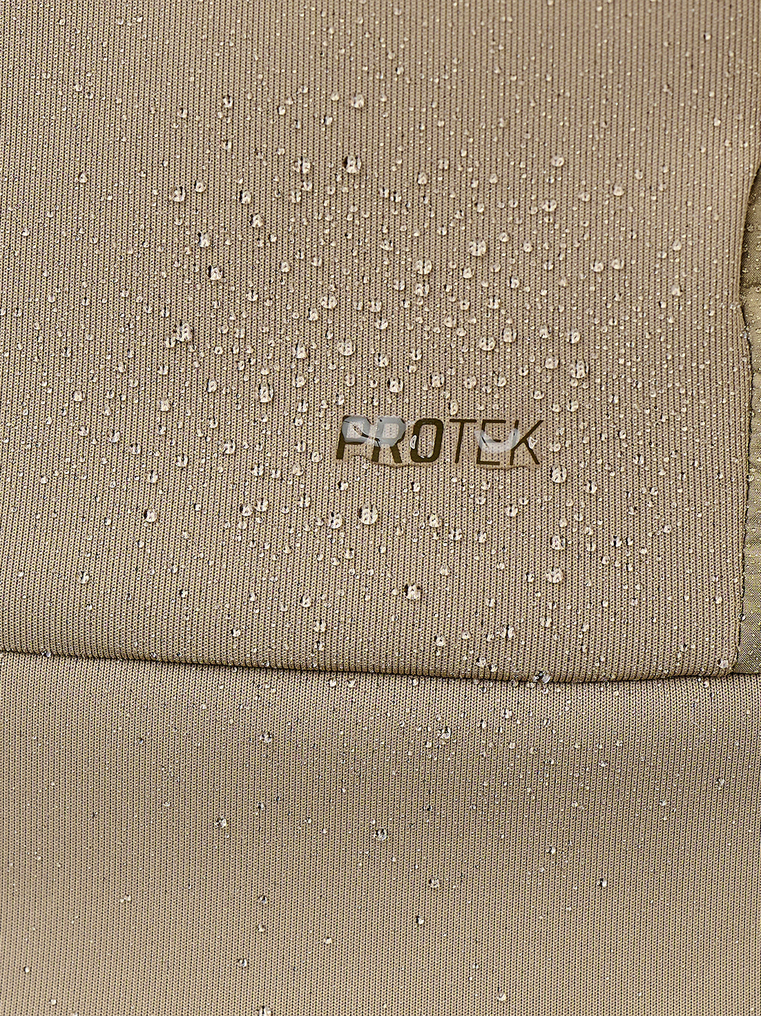 Close-up of a beige textured fabric with water droplets on the surface and the word PROTEK printed in the center.