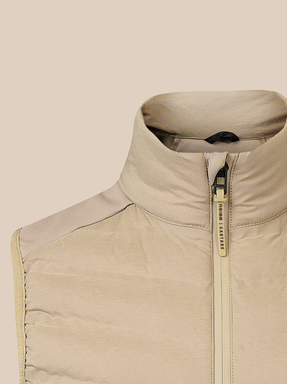 Close-up of a beige puffer vest with a high stand-up collar and a gold-tone zipper pull, shown against a solid beige background.