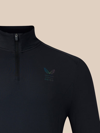 Close-up of a black long-sleeve quarter-zip athletic top with a small multicolor winged logo and the text 'CASTORE REISS' on the left chest, shown against a solid beige background.