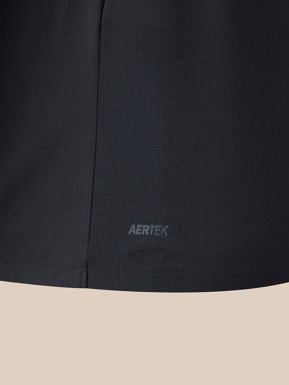 Close-up of a dark charcoal gray textured athletic fabric with the AERTEK logo embroidered near the bottom hem, set against a solid beige background.