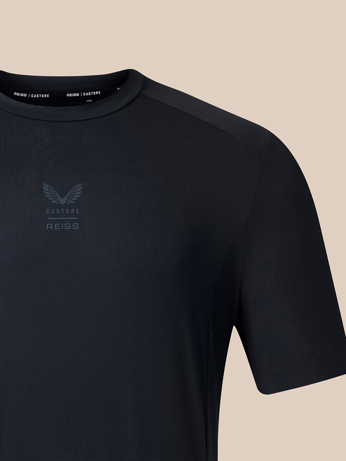 Close-up of a dark navy athletic short-sleeve shirt with a subtle tonal chest logo, shown against a solid beige background.