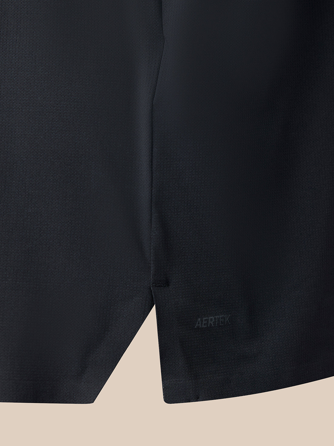 Close-up of a dark athletic fabric garment corner showing a small tonal AERTEK logo on a light beige background.
