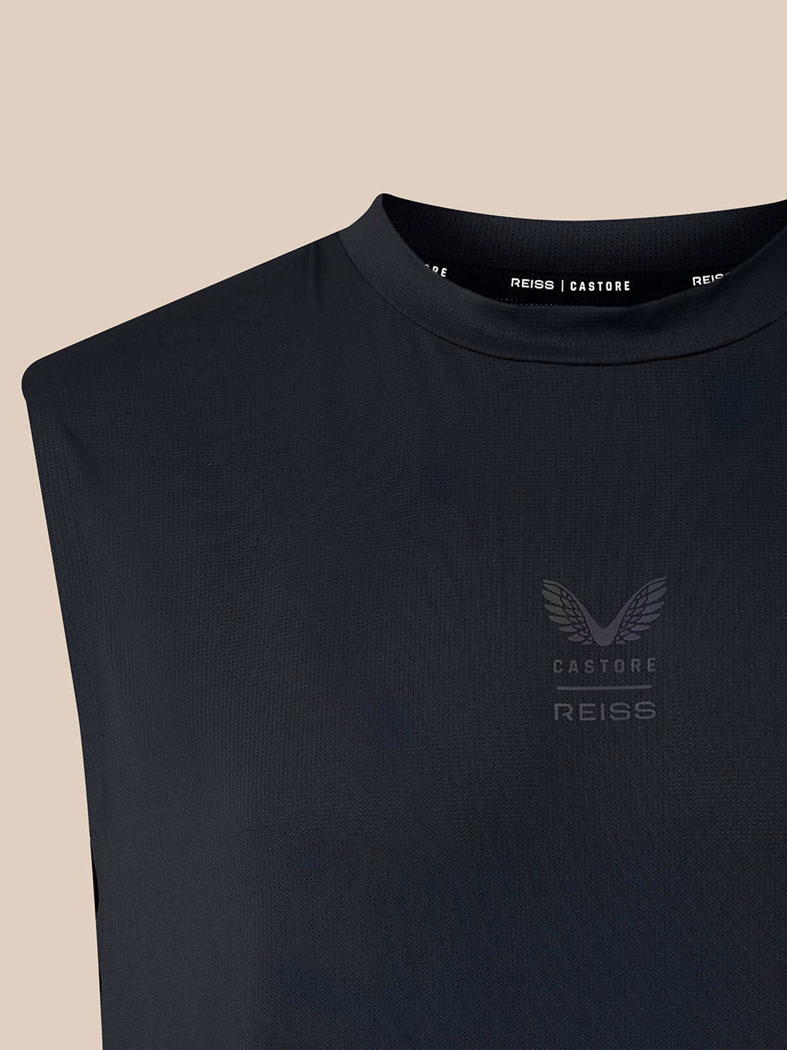 Close-up of a sleeveless black ribbed top with a crew neck and a subtle winged logo on the left chest, shown against a light beige background. The inner collar shows the brand name REISS | CASTORE.