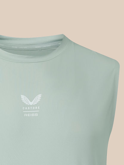 A close-up of a sleeveless ribbed top in a pale mint green color, featuring a white winged logo and the text 'CASTORE REISS' on the left chest, set against a solid beige background.