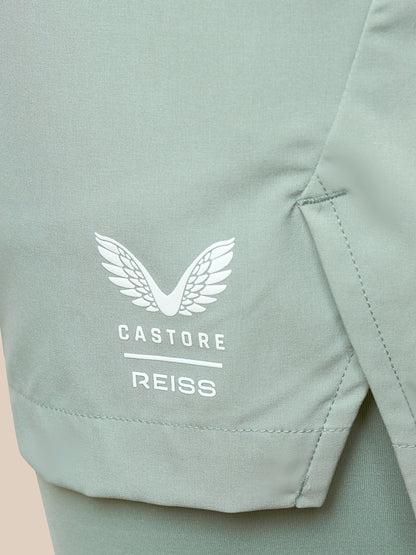 Close-up of a sage green athletic garment showing a white embroidered wing logo and the text 'CASTORE REISS' on the side.