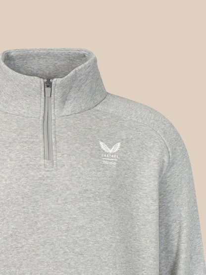 Close-up of a light heather gray quarter-zip pullover with a white embroidered winged logo and the word 'CASTORE' on the left chest, set against a solid beige background.