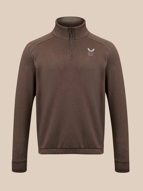 A brown long-sleeve quarter-zip pullover sweater with a small white winged logo on the left chest, displayed on a neutral beige background.