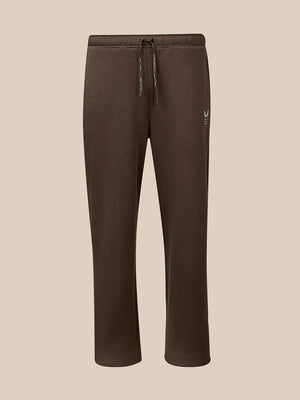 A pair of dark brown sweatpants with a drawstring waist and a small white embroidered logo on the left thigh, shown against a solid beige background.