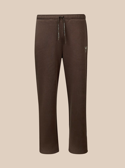 A pair of dark brown sweatpants with a drawstring waist and a small white embroidered logo on the left thigh, shown against a solid beige background.