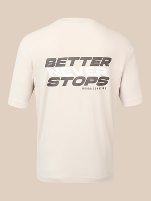 A cream-colored short-sleeve t-shirt shown from the back, featuring a large graphic print that reads 'BETTER NEVER STOPS' in gray and white, with 'REISS | CASTORE' printed below it, set against a solid beige background.