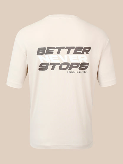 A cream-colored short-sleeve t-shirt shown from the back, featuring a large graphic print that reads 'BETTER NEVER STOPS' in gray and white, with 'REISS | CASTORE' printed below it, set against a solid beige background.