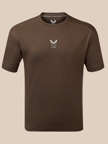 A dark brown short-sleeve crewneck t-shirt with a small white winged logo and 'Castore Reiss' text on the left chest, displayed on a neutral beige background.