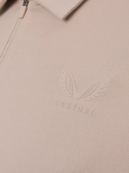 Close-up of a light beige zip-up jacket or sweater showing the collar, zipper pull, and an embossed winged logo with the word CASTORE on the chest.