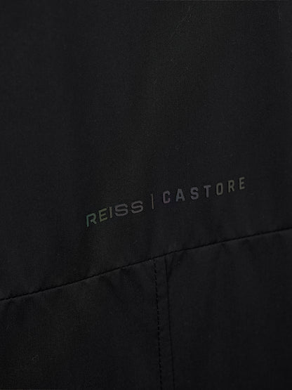 Close-up of a black garment with the REISS | CASTORE logo printed across the chest in a subtle iridescent tone.